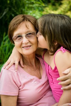 Lifestyle portrait of grandchild kissing grandmother - outdoor in nature