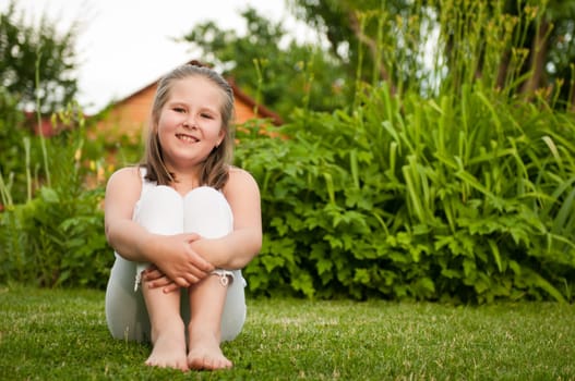 Backyard portrait of smiling child (nine years old girl) sitting on grass