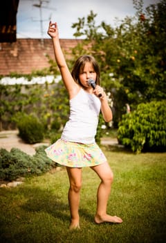 Happy childhood - child singing with microphone outdoor in backyard