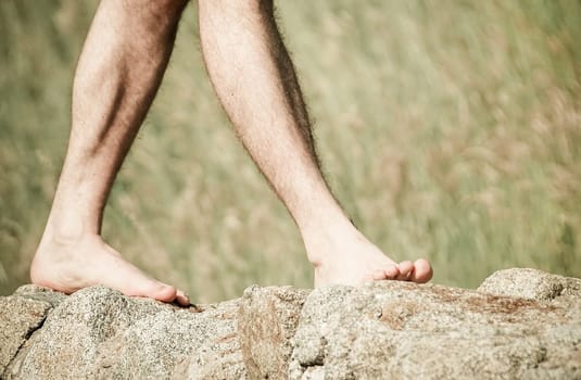 Legs of man on rocky wall with grass in the background