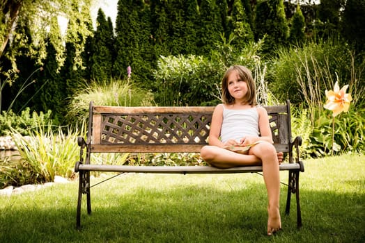 Daydreaming child portrait - little girl sitting on bench outdoor in backyard