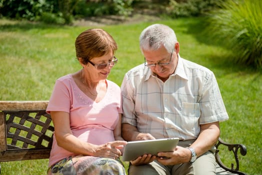 Lifestyle portrait of smiling happy senior couple working with tablet - outdoor