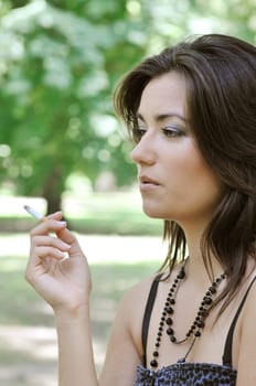 Portrait of young woman smoking cigarette outdoors in sunny green park