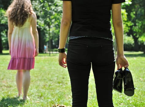 One woman stands turned back to her friend who holds shoes in hand