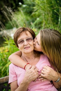 Lifestyle portrait of grandchild kissing grandmother - outdoor in nature