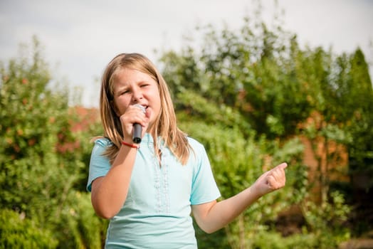 Happy childhood - child singing with microphone outdoor in backyard