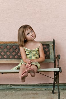 Portrait of cute child sitting on bench and stretching barefoot legs