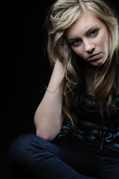 Young blond woman (teenager) in depression isolated on black background