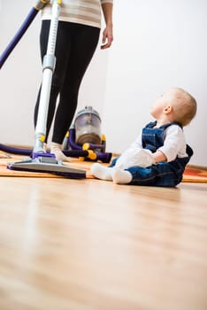 Cleaning up the room - woman with vacuum cleaner, baby sitting on floor