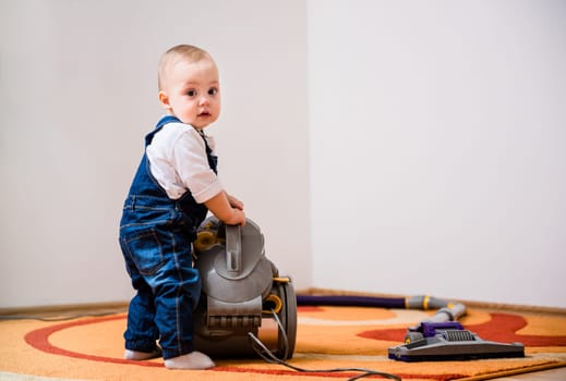 Little baby standing at vacuum cleaner - home interior