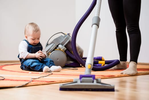 Cleaning up the room - woman with vacuum cleaner, baby sitting on floor