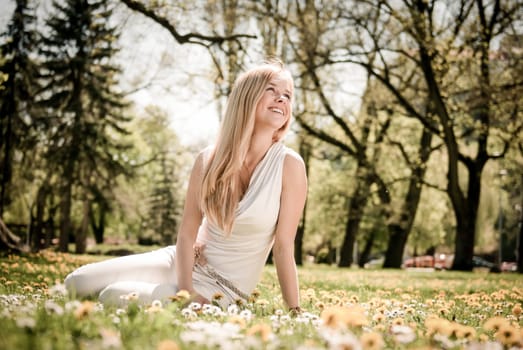 Smiling happy young person (teenager) sitting outdoors in blooming grassfiled and looking away