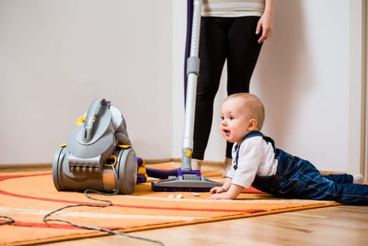 Cleaning up the room - woman with vacuum cleaner, baby sitting on floor