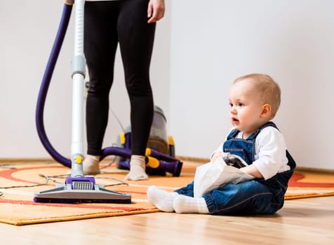 Cleaning up the room - woman with vacuum cleaner, baby sitting on floor