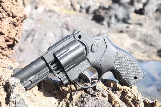 Plastic Revolver Gun Toy on the Volcanic Rocks