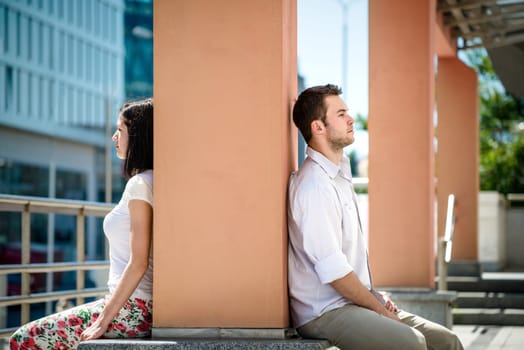 Couple having problems - two people sitting on opposite side of big collumn in street
