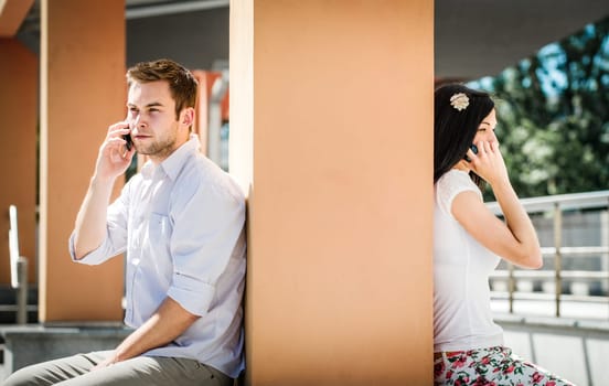 Couple having problems - two people sitting on opposite side of big collumn calling phone