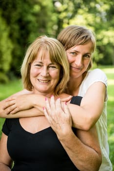 Outdoor portrait of smiling happy senior mother with her adult daughter