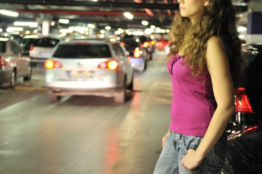 Young woman standing at car in underground parking place