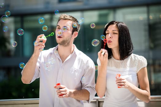 Young couple play together with bubble blower - outdoor in street