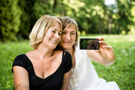 Adult daughter and her senior mother are taking picture with mobile phone