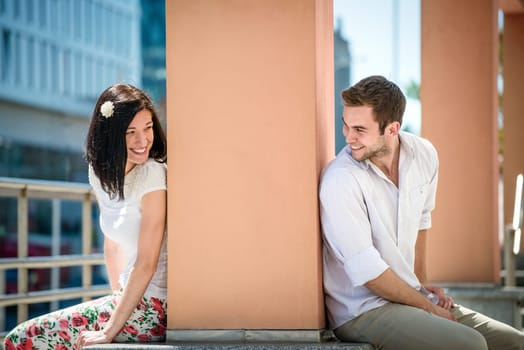 Two people sitting on opposite side of big collumn - outdoor in street