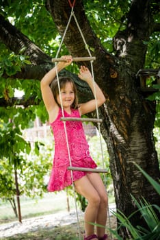 Happy child is playing on rope ladder outside in nature