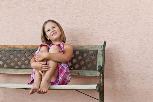 Portrait of cute smiling child sitting on bench and holding her legs
