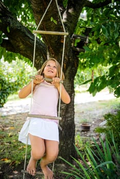 Happy child is playing on rope ladder outside in nature