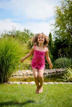 Active child - happy girl jumping with skipping rope outdoor in backyard