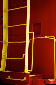 A bright yellow steel ladder on a bright red vintage train caboose.