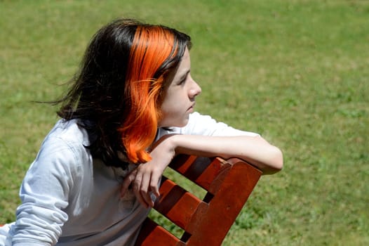 Boy sitting on bench looking right and back, grass background