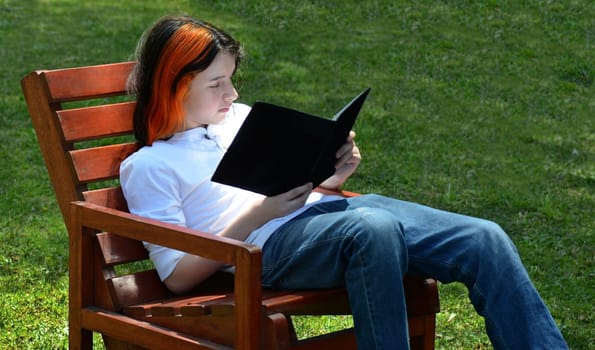 Boy reading on bench looking right, grass background