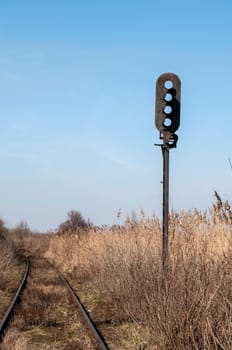 Abandoned rail line and empty railway traffic light in dry grass field