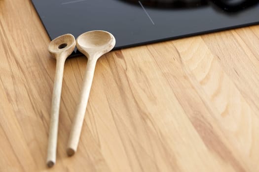 Two wooden spoons lie in front of a ceramic hob