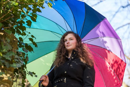 A young pretty woman stands with a colorful umbrella in the winter sun