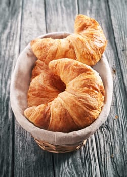 High angle view of freshly baked flaky golden croissants in a basket served on an old rustic wooden table with a weathered texture