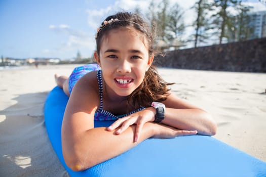 Closeup portrait of cute young girl lying on blue surfboard on the beach