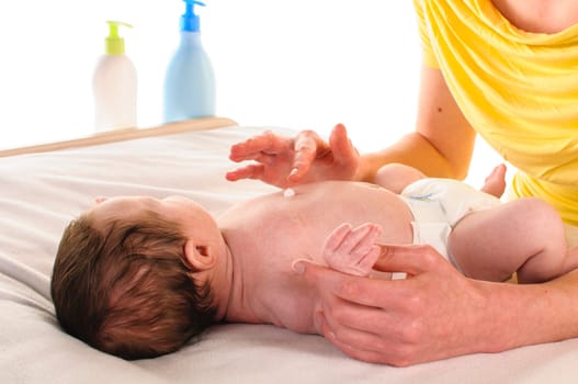 Mother with her newborn baby does infant care at the changing table,exposed against a white background.
