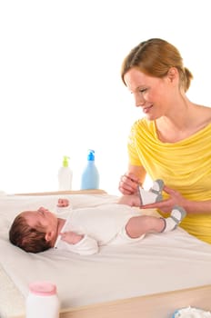 Mother with her newborn baby does infant care at the changing table,she puts socks on the baby,exposed against a white background.