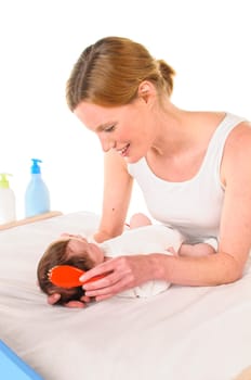 Mother with her newborn baby does infant care at the changing table,she tenderly brushes the hair,exposed against a white background.