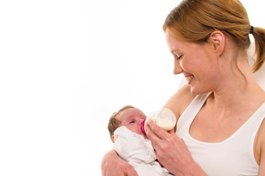 An adult woman with a white shirt tenderly holds an infant,also dressed in white,in her arms and gives him his bottle,exposed against a white background.