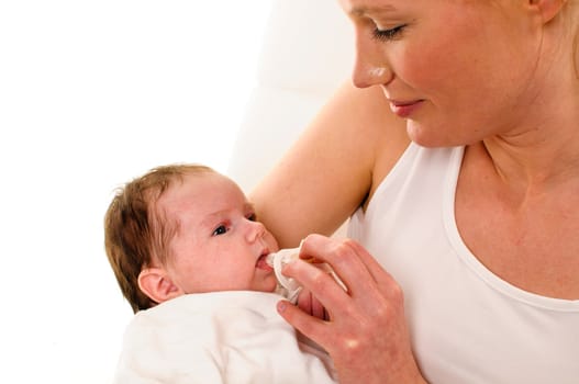 An adult woman with a white shirt holds an infant dressed in white tenderly in her arms,she gives him a teat,exposed against a white background.