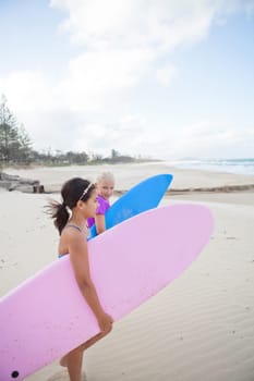 Two cute young girls walking together towards ocean with surfboards at the beach