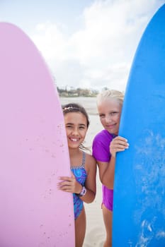 Two cute smiling young girls holding surfboards upright at the beach