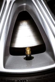 close-up of a tire valve on car wheel with visible aloy wheel and a fragment of brake disc.