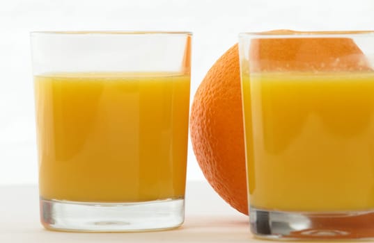 Two glasses of orange juice and one orange against a white background