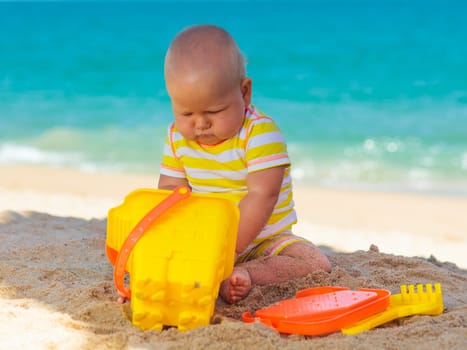 Cute baby on the tropical beach playing toys
