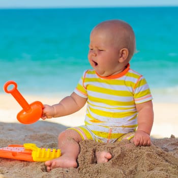 Cute baby on the tropical beach playing toys
