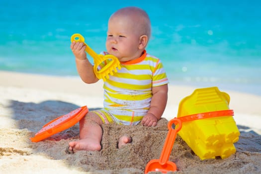 Cute baby on the tropical beach playing toys